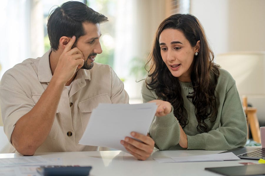 A man and woman sit at a table, reviewing documents together. The man listens attentively while the woman points at the papers, discussing something important.