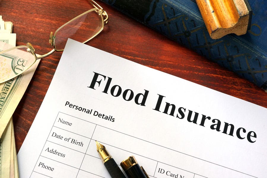 A flood insurance form on a desk with a pen, glasses, cash, and a book nearby, ready to be filled out—perfect for exploring insurance discounts through bundling insurance policies.