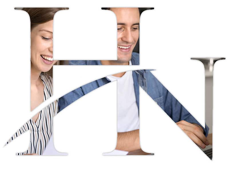 Two people smiling and working together on a laptop, visible through a large, stylized HN logo with a diagonal line cutting through the letters.