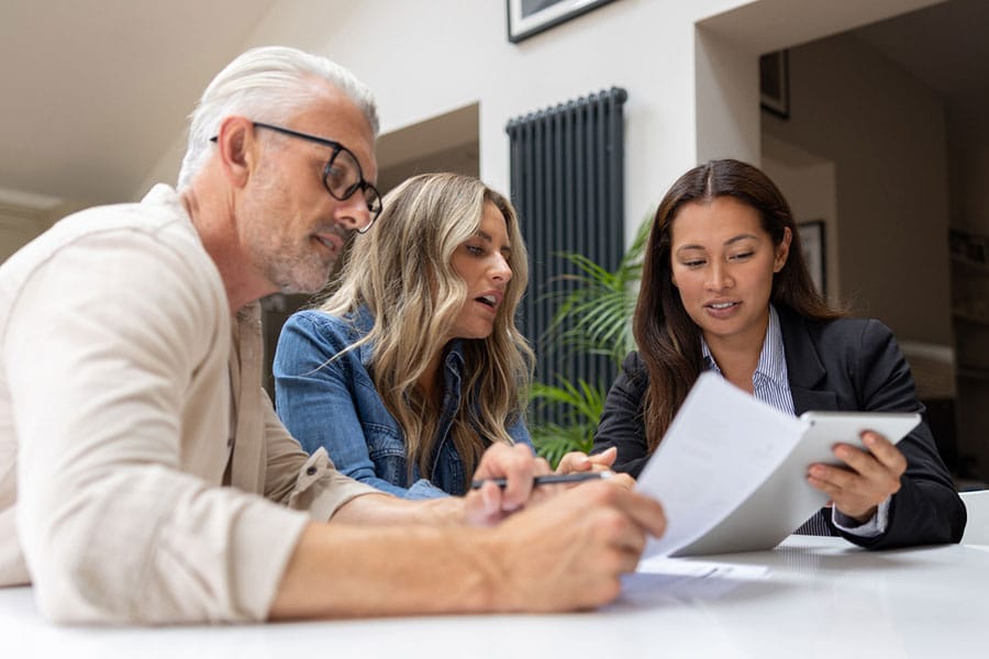 Three people sit at a table, discussing documents related to small business policies. One woman holds a tablet, another looks at papers, while a man listens attentively. They appear to be in a bright, modern office or home setting—focused on protecting your business and ensuring everything runs smoothly.