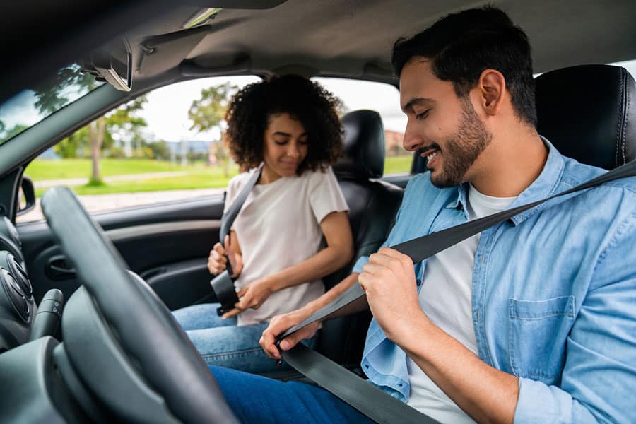 A man and woman sitting in a car, smiling and fastening their seat belts. Trees and grass are visible outside the windows, suggesting they are parked or about to drive in a suburban or park area—perhaps after visiting one of Metro Detroit’s trusted Independent Car Insurance Agents. A man and woman sitting in a car, smiling and fastening their seat belts. Trees and grass are visible outside the windows, suggesting they are parked or about to drive in a suburban or park area—perhaps after visiting one of Metro Detroit’s trusted Independent Car Insurance Agents.