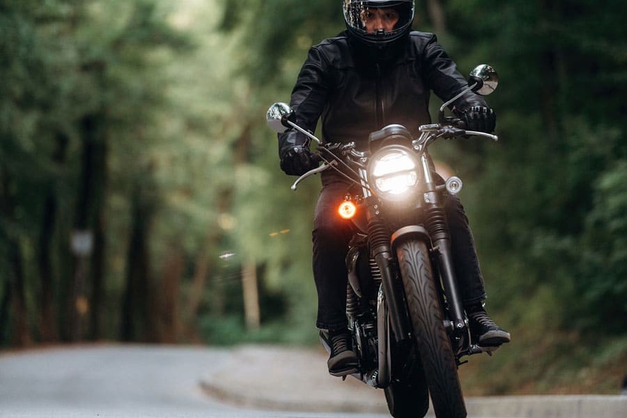 A person wearing a helmet and black jacket rides a motorcycle on a winding road through a green forest, embodying the freedom Metro Detroit riders enjoy—especially with peace of mind from independent agents specializing in motorcycle insurance.